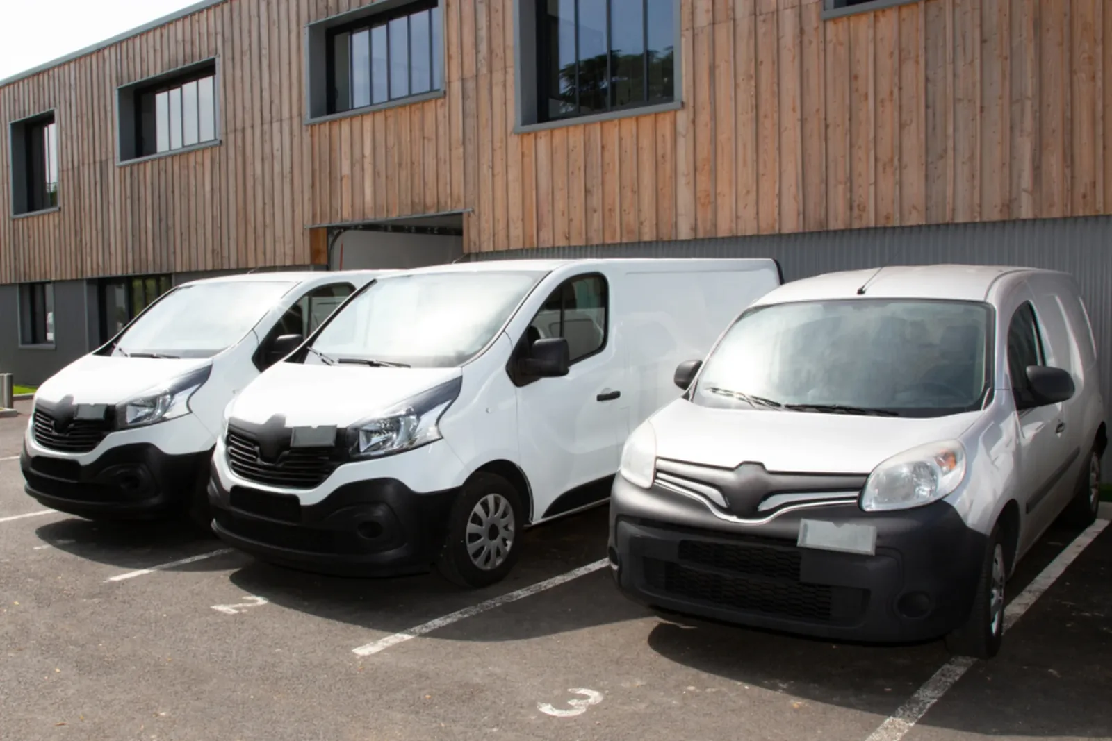 Row of white commercial vans parked outside a workshop building.