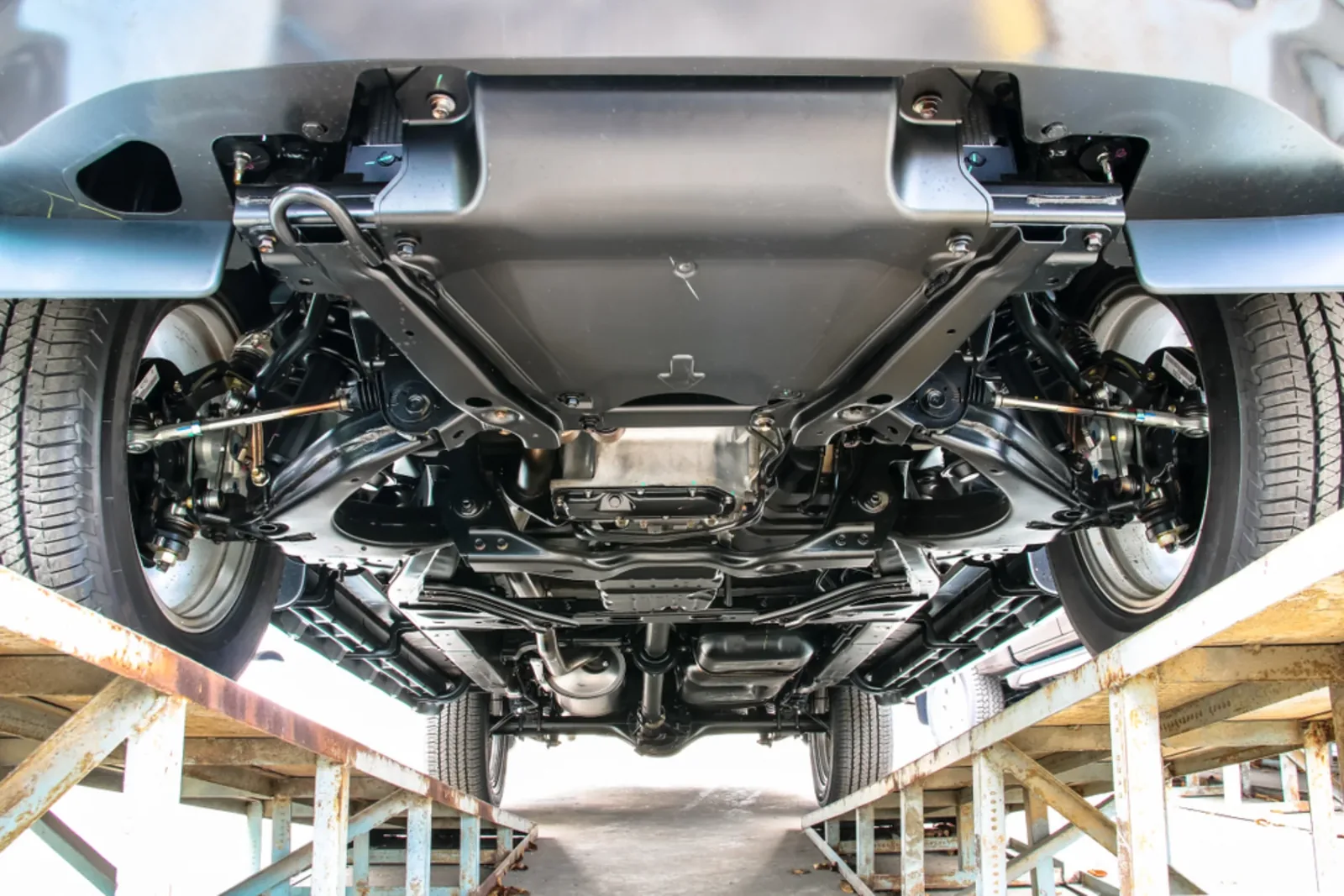 Wide view of a vehicle raised on a workshop hoist with its underbody exposed.
