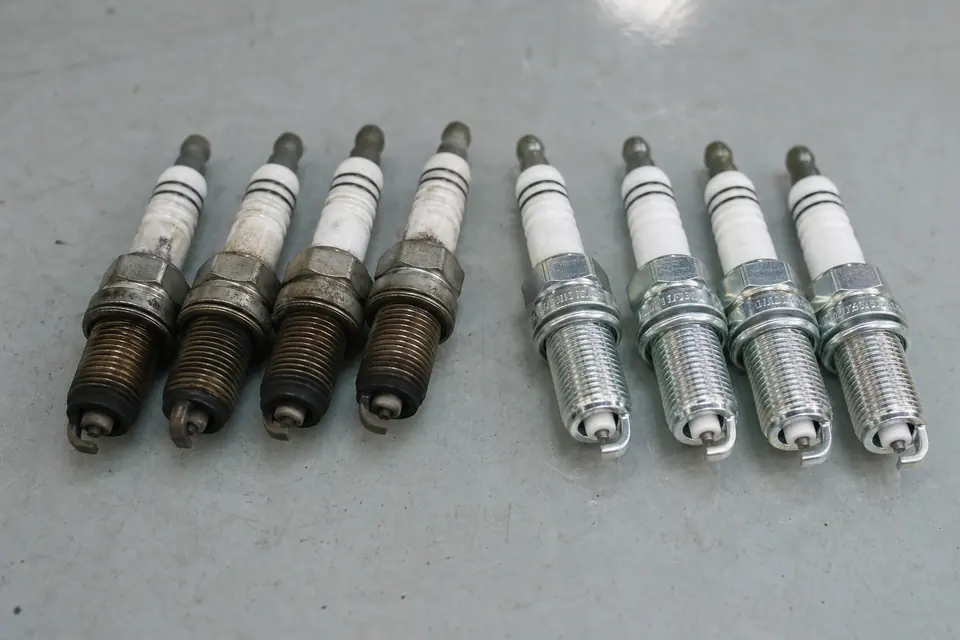 Four worn and four new spark plugs arranged side by side