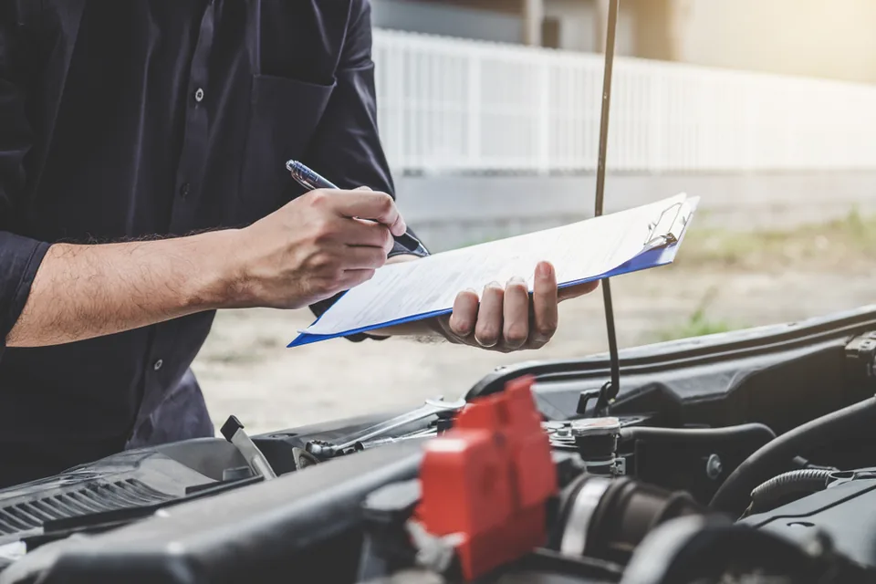 Mechanic writing on a clipboard beside a vehicle with its bonnet open.