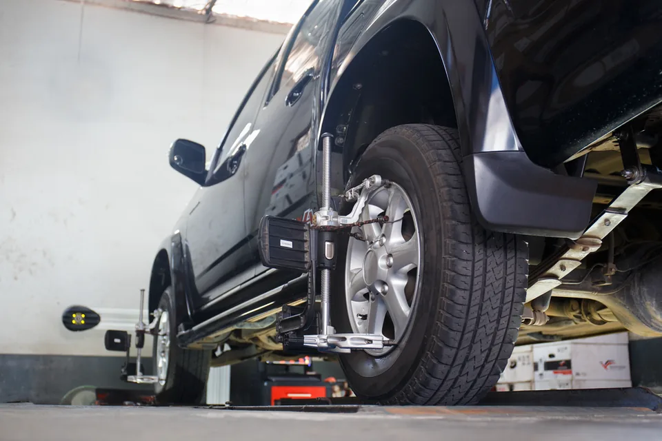 Vehicle raised on a hydraulic hoist with a wheel removed in a workshop bay.